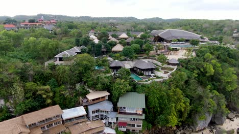 Tropical-exotic-resort-villa-complex-on-Bali-coastline,-aerial-drone-fly-backward-view