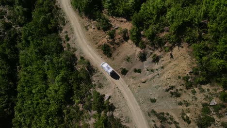 Drone-footage-looking-down-on-a-white-camper-van-winding-its-way-along-a-dirt-trail-in-the-Trebeshinë-Dhëmbel-Nemërçkë-mountain-chain-near-Permet,-Albania