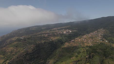 Aerial-view-of-the-Calheta-parish-in-the-Madeira-Island-Portugal,-Drone-rotating-to-the-right-showing-the-the-house-on-the-top-of-the-mountain-and-some-mist-passing-thru-the-camera