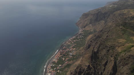 Vista-Aérea-De-La-Parroquia-Calheta-En-La-Isla-De-Madeira,-Drone-Girando-Mostrando-El-Contraste-Entre-El-Pueblo-Cerca-Del-Mar-Y-Las-Montañas-En-El-Fondo