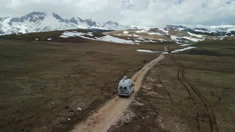 Aerial-slowly-follows-camper-van-on-dirt-road-in-mountains,-Montenegro