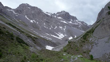 Aerial-drone-footage-slowly-reversing-and-rising-to-reveal-a-glacial-mountain-landscape-with-patches-of-snow,-isolated-trees-a-remote-alpine-hiking-trail-in-Switzerland