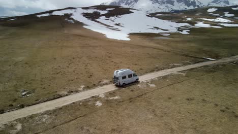 Aerial-panning-of-camper-van-driving-through-snowy-plateau,-Montenegro