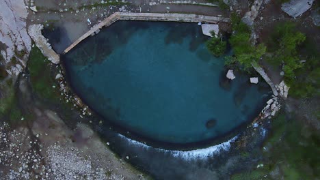Drone-looking-straight-down-at-the-turquoise-water-of-the-Benja-thermal-pool-in-Permet,-Albania