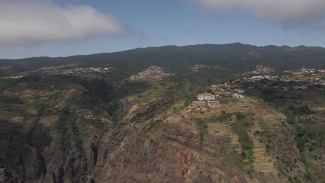 Aerial-view-of-the-Calheta-parish-in-the-Madeira-Island-Portugal,-Drone-rotating-to-the-right-showing-the-the-houses-on-the-top-of-the-mountain-and-some-clouds-in-the-background