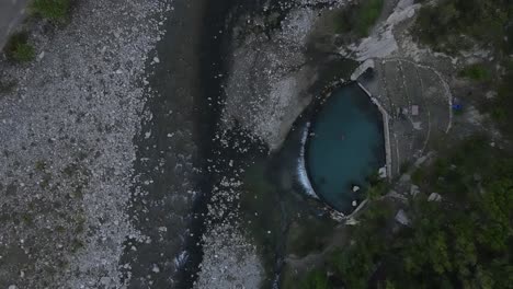 Drone-footage-looking-straight-down-at-Benja-Thermal-Pool-with-the-Vjosa-river-flowing-past-in-Albania