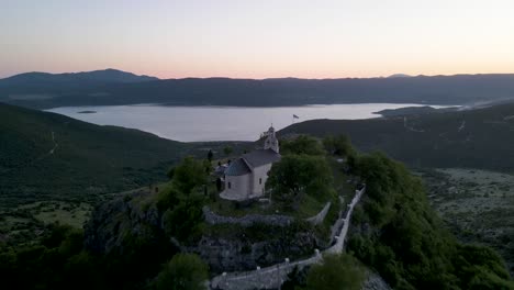 Fliegen-Sie-über-Die-Kirche-Und-Enthüllen-Sie-Den-Wunderschönen-See-Bei-Sonnenuntergang,-Montenegro
