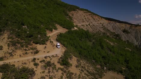Drone-footage-of-a-white-camper-van-driving-down-Trebeshinë-Dhëmbel-Nemërçkë-mountainside-near-Permet,-Albania