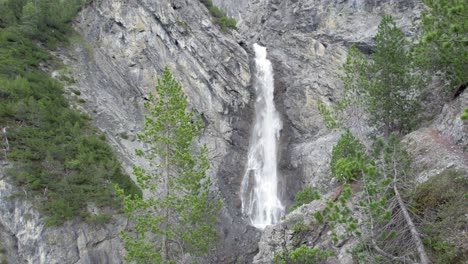 Drohnenaufnahmen-Aus-Der-Luft,-Die-Langsam-Durch-Ein-Baumkronendach-Auf-Einen-Dramatischen-Wasserfall-Zufliegen,-Der-über-Den-Rand-Einer-Steilen-Bergklippe-In-Der-Schweiz-Kaskadiert