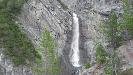 Drohnenaufnahmen-Aus-Der-Luft,-Die-Langsam-über-Einem-Baumdach-Aufsteigen,-Um-Einen-Dramatischen-Wasserfall-Zu-Enthüllen,-Der-über-Den-Rand-Einer-Steilen-Bergklippe-In-Ein-Tauchbecken-In-Der-Schweiz-Stürzt
