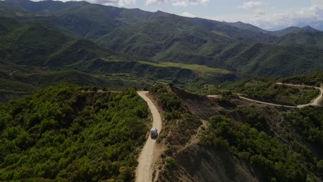 Drone-footage-flying-over-a-camper-van-driving-along-a-winding-dirt-road-in-the-Trebeshinë-Dhëmbel-Nemërçkë-mountain-chain-near-Permet,-Albania