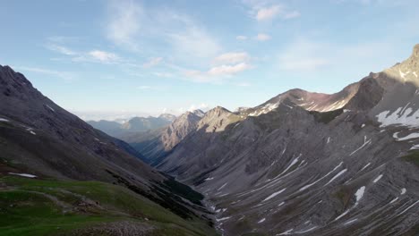 Aerial-drone-footage-slowly-flying-upwards-through-a-dramatic,-jagged-mountain-landscape-with-residual-patches-of-snow-and-alpine-meadows-looking-down-through-a-glacial-valley-in-Switzerland