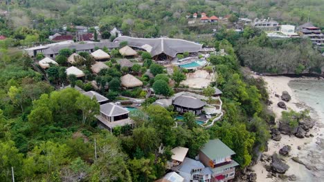 Luxury-villa-resort-on-rocky-coastline-of-Padang-Padang-in-Bali,-aerial-orbit-view