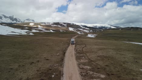 Flyover-of-camper-van-driving-on-dirt-road-in-open-plateau,-Montenegro