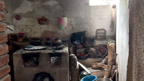Inside-Rural-Rustic-Old-Kitchen-in-Countryside-Region,-Cement-Traditional-Wood-Coal-Fire-Stove-Cooktop,-Dishes-Pans-Pots-and-Pottery-Scattered-Around,-Interior-Antique-and-Poverty,-Dolly-View