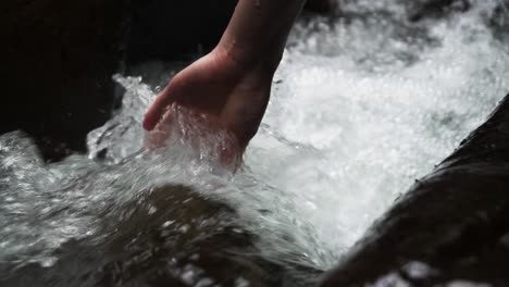 Person-puts-their-hand-in-fast-flowing-stream-of-water-as-it-passes-between-rocks