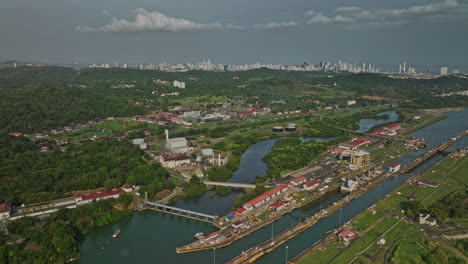 Panama-City-Aerial-v36-high-angle-view-of-miraflores-lake-and-cargo-ships-at-locks-canal,-waiting-for-sluice-gate-to-open-with-cityscape-in-distance-background---Shot-with-Mavic-3-Cine---March-2022