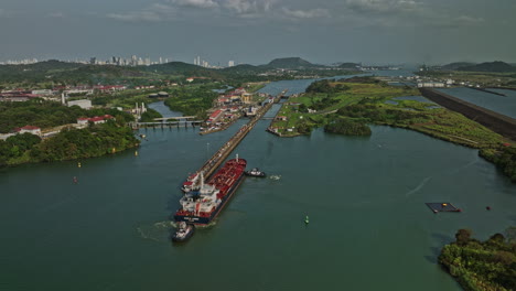 Panama-City-Aerial-v31-pull-out-shot-of-cargo-tanker-ship-transiting-at-canal-locks-towards-pacific-ocean-from-miraflores-lake-with-cityscape-in-the-skyline---Shot-with-Mavic-3-Cine---March-2022