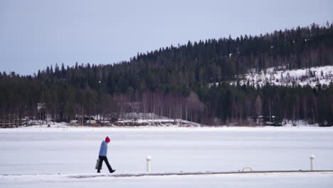 A-single-person-walking-in-the-snow-with-bright-bobble-hat-in-Vuokatti-Finland,-left-to-right