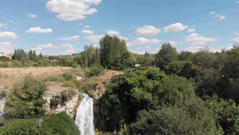 Rising-drone-shot-looking-towards,-then-beyond-El-Hundimiento-waterfall-at-Lagunas-de-Ruidera,-Spain