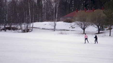 Two-people-in-warm-winter-clothes-skiing-past-on-vast-snowy-area-towards-a-large-forest-area-in-Vuokatti-Finland