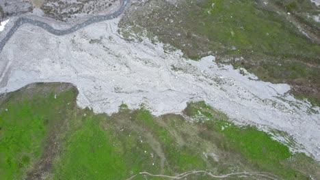 Luftaufnahmen-Von-Drohnen,-Die-Sich-Langsam-In-Richtung-Eines-Windigen-Grauen-Flussbetts-Und-Einer-Grasbewachsenen-Grünen-Alpenwiese-In-Den-Bergen-Der-Schweiz-Winden