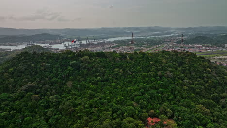 Panama-City-Aerial-v23-cinematic-drone-flyover-ancon-hill-with-national-flag-waving-on-hilltop,-reveals-water-canal,-industrial-shipyard-and-international-airport---Shot-with-Mavic-3-Cine---March-2022