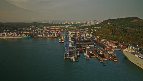 Panama-City-Aerial-v46-panning-view-capturing-port-of-balboa-large-container-terminal-and-shipyard-with-ancon-hill-and-cityscape-in-the-background-at-sunset---Shot-with-Mavic-3-Cine---March-2022
