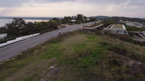 Aerial-tracking-shot-of-cyclist-riding-mountain-bike-uphill-slope-road-along-coastline-of-Ocean-in-Uruguay