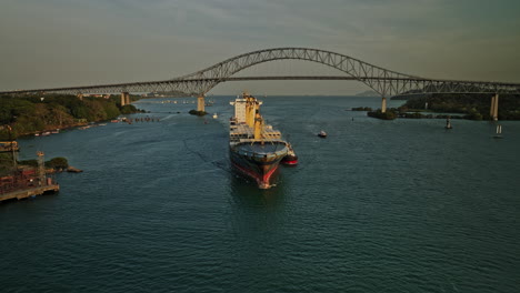 Panama-City-Aerial-v52-cinematic-reverse-flyover-the-water-canal-capturing-cargo-carrier-ship-with-bridge-of-americas-in-the-background-at-sunset-golden-hours---Shot-with-Mavic-3-Cine---March-2022
