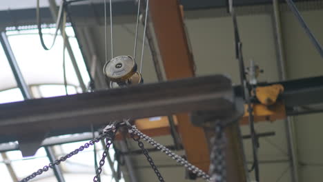 A-hoist-carrying-up-in-the-air-a-heavy-load-inside-an-industrial-hall,-motion-of-metal-flying-with-scenery