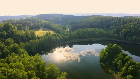 Aerial-view-of-a-beautiful-Polish-lake-surrounded-by-lush-forest-with-the-sun-reflecting-on-the-water