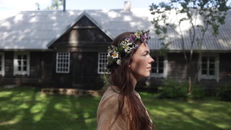 A-woman-with-the-flower-crown-is-walking-by-an-ancient-cottage-as-the-camera-is-following-her,-natural-colour,-slow-motion