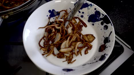 Golden-Brown-Crispy-Fired-Sliced-Onions-Being-Placed-On-A-Plate