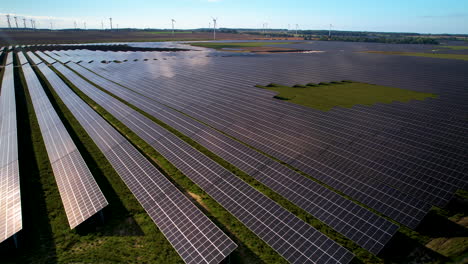 Aerial-Closeup-Of-Field-Of-Solar-Panels-With-Wind-Turbines-At-Background