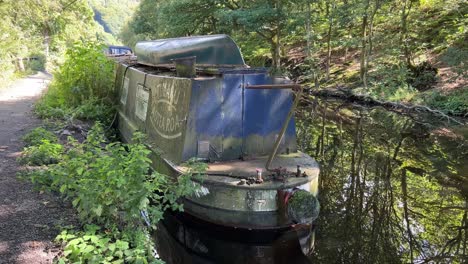 Old-abandoned-barge,-river-boat,-longboat,-in-a-woodland-setting-on-a-Canal-in-West-Yorkshire,-England