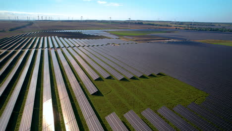 Aerial-View-Of-A-Vast-Solar-Farm-Panels-With-Wind-Turbines-At-Background