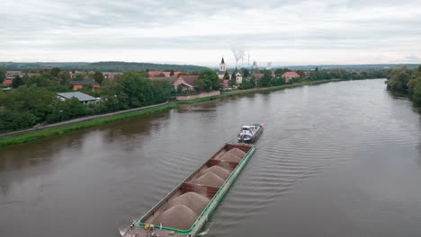 Aerial-shot-of-a-tugboat-pushing-a-load-of-sand-down-the-Elbe
