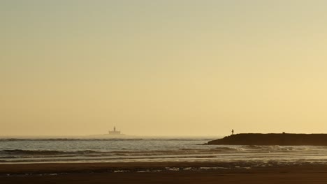 Silhouette-of-lonely-fisherman-fishing-on-a-sea-breakwater-at-sunset,-wide-shot