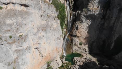 Tilt-down-shot-of-Salto-de-los-Órganos-waterfall,-as-clean-water-cut-through-the-rocks-forming-a-pond-at-the-bottom-of-the-cliffs