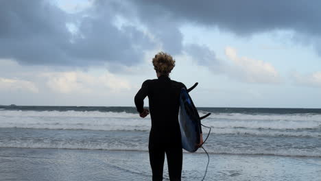 Boy-with-his-surfboard-and-at-dawn-enters-the-ocean-to-surf-the-waves