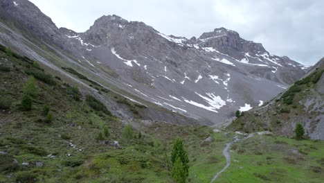 Luftdrohnenaufnahmen,-Die-Langsam-Durch-Eine-Eiszeitliche-Berglandschaft-Mit-Schneeflecken,-Vereinzelten-Bäumen-Fliegen,-Ein-Abgelegener-Alpiner-Wanderweg-In-Der-Schweiz