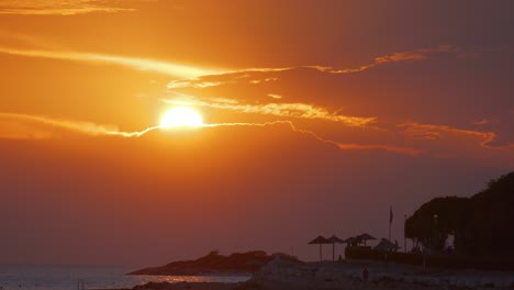 Sunset-in-croatia-sun-falling-into-the-sea-over-a-red-orange-sky-silhouette-of-umbrellas
