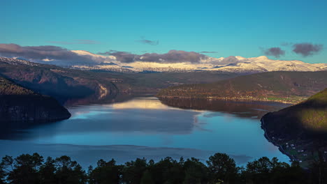 Ein-Atemberaubender-Blick-Auf-Einen-Großen-Fjord-In-Norwegen---Tageszeitraffer-Mit-Einem-Boot-Auf-Dem-Wasser-Und-Einer-Wolkenlandschaft-über-Den-Fernen-Schneebedeckten-Bergen