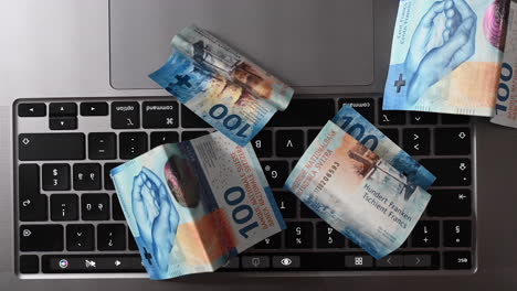 Top-view-of-100-bucks-bank-notes-on-a-laptop-keyboard,-profit-made-on-the-internet-with-an-online-business,-swiss-francs
