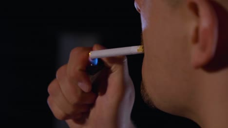 Close-up-shot-of-a-person-lighting-a-cigarette-from-behind-with-a-black-background,-slow-motion