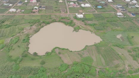 AERIAL---Brown-lake-and-town-in-Jos-Plateau,-Nigeria,-forward-tilt-down-shot