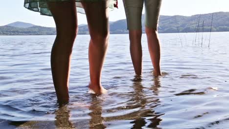 Couple-is-dipping-their-feet-in-a-shallow-lake-water-near-the-coast-line