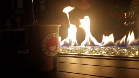Close-up-steaming-hot-coffee-in-a-design-plastic-cup-in-front-of-a-fire
