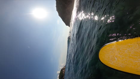 Bright-sun-reflects-on-ocean-water-while-person-surfing,-vertical-POV-slow-motion